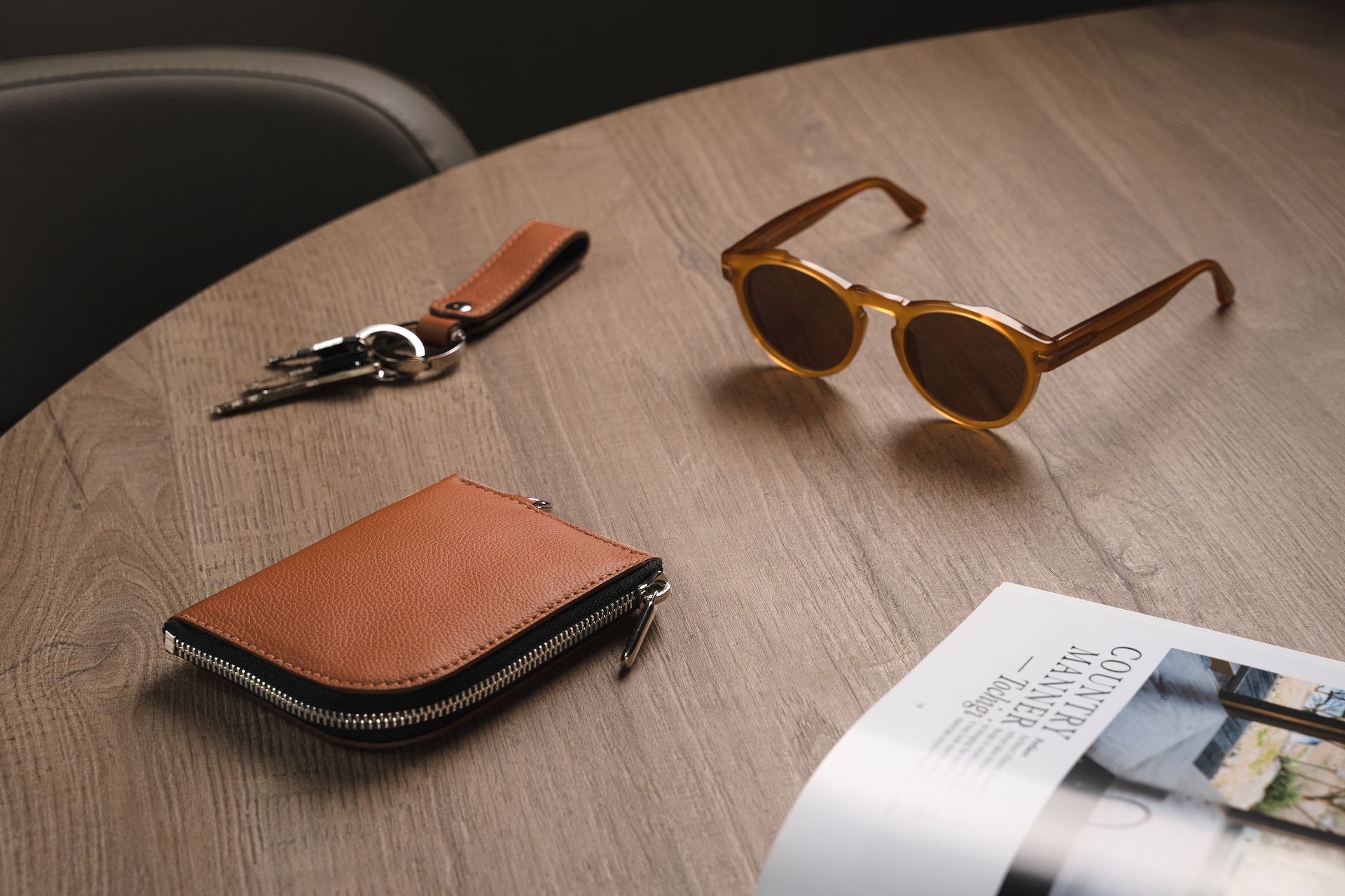 une table comportant des clés, une paire de lunette de soleil, un magazine et un porte carte en cuir marron